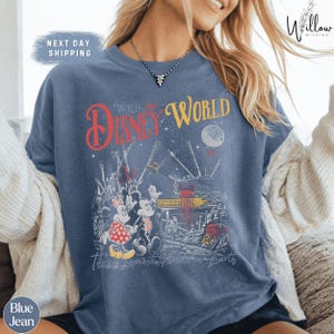 A woman wearing a blue t-shirt with a Disney World-themed graphic printed on it.