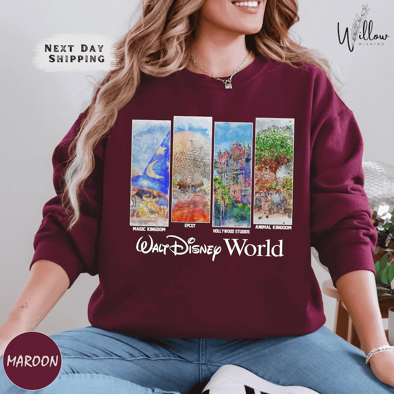 A woman wearing a maroon sweater with a graphic design featuring four panels depicting scenes from Walt Disney World, including Magic Kingdom, Epcot, Hollywood Studios, and Animal Kingdom.