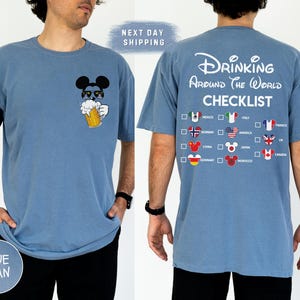 May include: Blue jean t-shirt featuring a Mickey Mouse graphic wearing sunglasses and holding a beer mug. The back of the shirt displays the text "Drinking Around The World Checklist" with country flags and check boxes.