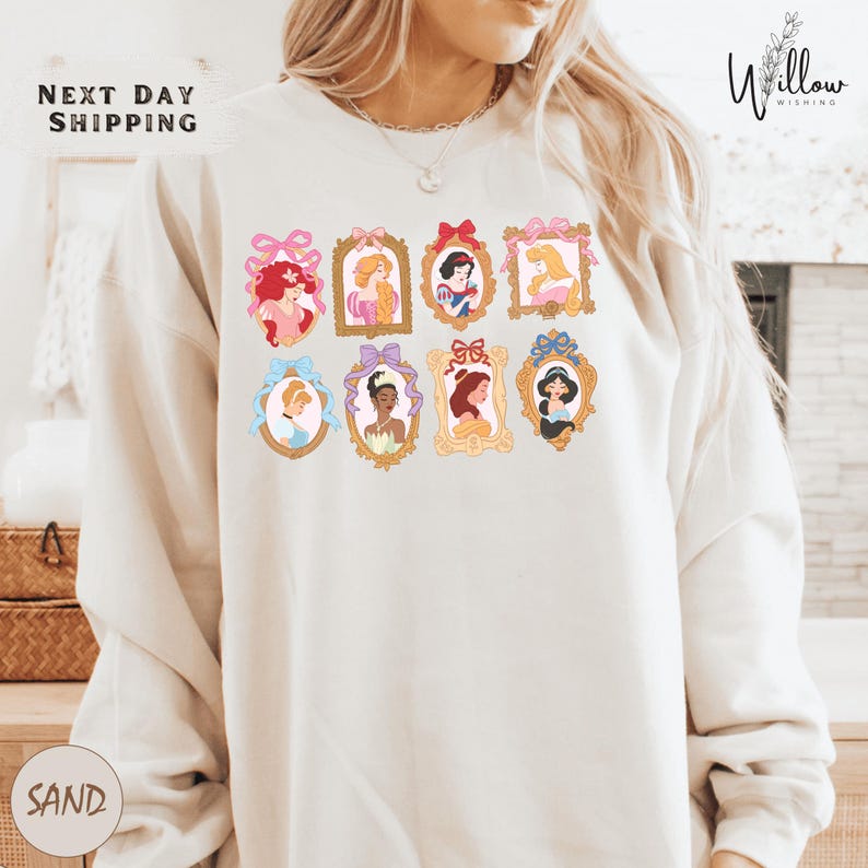 A woman wearing a white sweatshirt with a graphic design of various Disney princesses in frames.