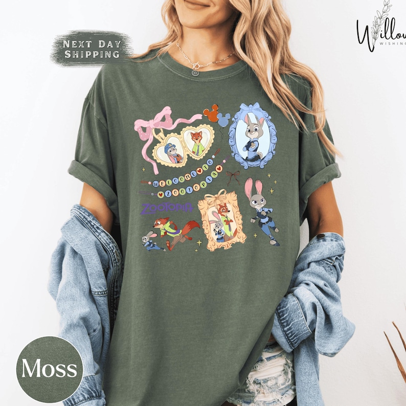 A woman wearing a green t-shirt with a cartoon character design, including a rabbit, a cat, and other animals. She is also wearing a denim jacket and has her arms around her shoulders.