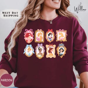A woman wearing a burgundy sweater with a collage of illustrations of Disney princesses.