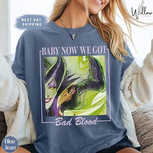 A woman wearing a blue t-shirt with a graphic design featuring a character from the Disney movie "Bad Blood".