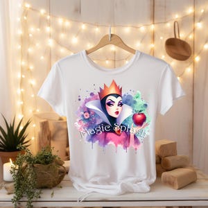 Puede incluir: Camiseta blanca con una ilustraci&oacute;n en acuarela de una reina con corona, sosteniendo una manzana roja. El dise&ntilde;o incluye el texto "Magic Splash" en una fuente de escritura, con salpicaduras de pintura coloridas.