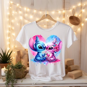 K&ouml;nnte beinhalten: Wei&szlig;es T-Shirt mit einem blauen und rosafarbenen Aquarell-Herz-Design mit Stitch und Angel aus Lilo & Stitch. Die Figuren k&uuml;ssen sich und sind von rosa und blauen Aquarell-Spritzen umgeben.