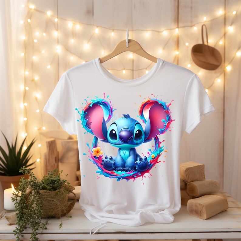 May include: White t-shirt with a blue Stitch character from Lilo & Stitch. Stitch is surrounded by colorful paint splatters in the shape of Mickey Mouse ears.