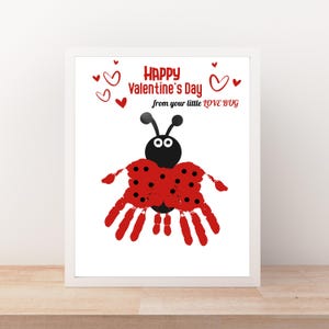 Op de afbeelding: Een ingelijste Valentijnsdag print met een lieveheersbeestje ontwerp gemaakt van handafdrukken. Het lieveheersbeestje heeft een zwarte kop en rode vleugels met zwarte stippen. De tekst luidt "Happy Valentine's Day from your little LOVE BUG" met rode harten.