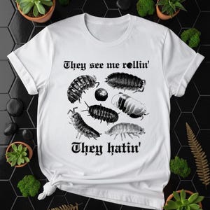 Puede incluir: Camiseta blanca con un gráfico negro de varios insectos y el texto "They see me rollin'" arriba y "They hatin'" abajo. Los insectos están dibujados con un estilo de ilustración vintage.
