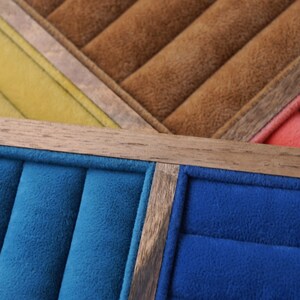 May include: A jewelry display tray featuring multiple rectangular sections lined with soft velvet in shades of blue, brown, yellow, and red. The sections are separated by thin, light-colored wooden dividers, creating organized slots for rings.