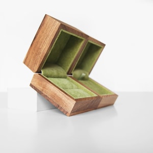 May include: Two wooden ring boxes with green velvet interiors. The boxes are open and stacked on top of each other.
