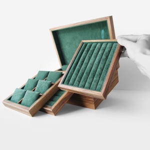 Può includere: Un sistema modulare per riporre gioielli con una cornice in legno marrone scuro e un interno in velluto verde smeraldo. Il set include un vassoio espositore per anelli con diverse fessure e un vassoio per orologi con scomparti imbottiti.