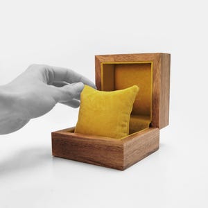 May include: A wooden box with a hinged lid, lined with a yellow velvet cushion. The box is open and the cushion is visible.