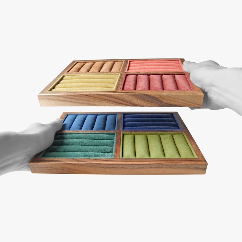May include: Two stacked wooden jewelry display trays featuring multiple velvet-lined compartments. The top tray contains orange, yellow, and red inserts, while the bottom tray features blue, dark blue, teal, and light green velvet ring rolls.