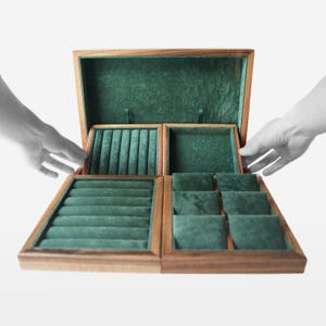 May include: A wooden jewelry box with a hinged lid, open to reveal multiple compartments lined with green velvet. The box has a natural wood finish and is designed to store various types of jewelry. The compartments include ring slots and open spaces.