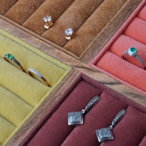 May include: A jewelry organizer tray with velvet-lined compartments containing two gold stud earrings with clear stones, two gold rings with green and clear stones, one silver ring with a green stone, and two silver drop earrings with square pendants.
