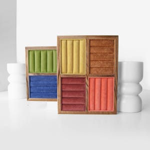 May include: Two rectangular wooden jewelry display organizers featuring multiple velvet-lined slots. One organizer has green and blue sections, while the other contains yellow, brown, dark red, and coral-colored velvet inserts for rings or earrings.