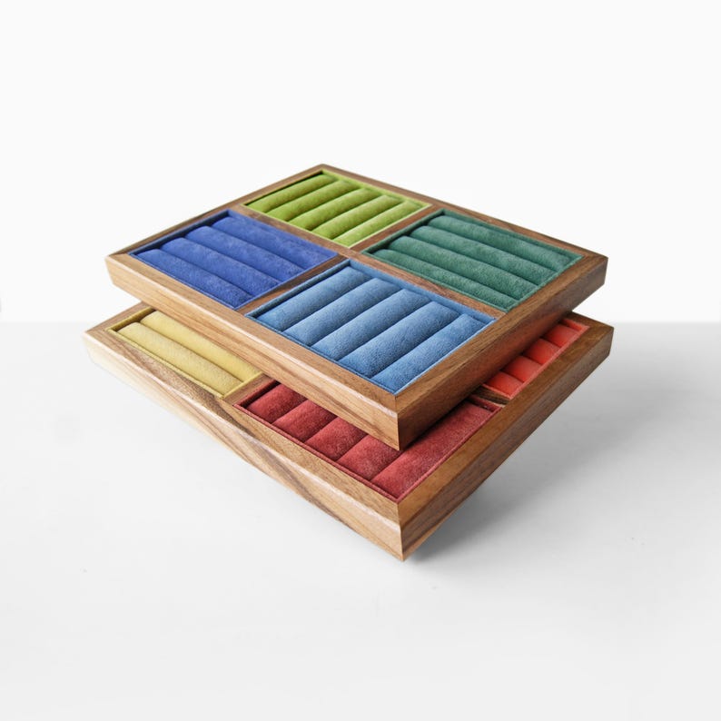 May include: Two stacked rectangular wooden jewelry display trays featuring multiple velvet-lined slots. The top tray contains sections in lime green, dark blue, forest green, and light blue. The bottom tray features yellow and red velvet inserts.