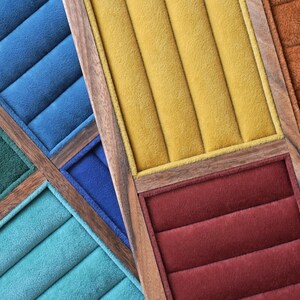 May include: A multi-compartment jewelry display tray featuring a wooden frame and soft velvet inserts in various colors including mustard yellow, deep red, royal blue, teal, and forest green, each section containing parallel padded ring slots.