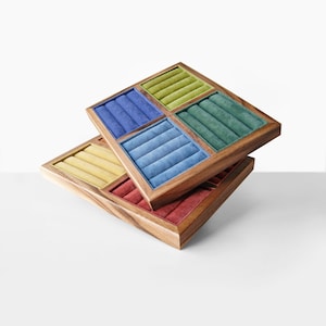 May include: Two stacked square wooden jewelry display trays featuring multiple velvet-lined ring slots. The top tray contains sections in lime green, dark blue, teal, and light blue. The bottom tray features yellow and red velvet inserts.