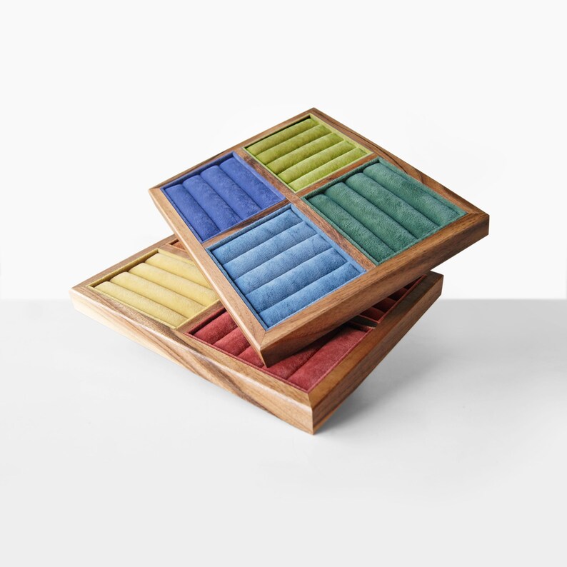 May include: Two stacked square wooden jewelry display trays featuring multiple velvet-lined ring slots. The top tray contains sections in lime green, dark blue, teal, and light blue. The bottom tray features yellow and red velvet inserts.
