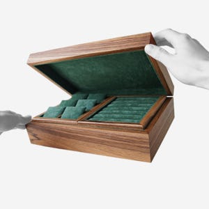 May include: Wooden jewelry box with a hinged lid, open to reveal a green velvet interior with compartments for rings and other jewelry. The box is made of a dark wood with visible grain.