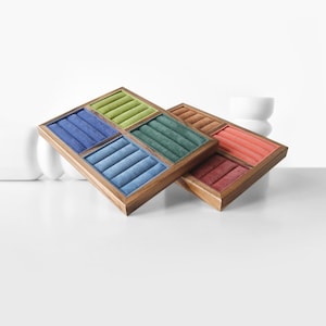 May include: Two rectangular wooden jewelry display trays featuring multiple velvet-lined ring slots. The first tray contains sections in blue, light blue, green, and lime green. The second tray features sections in brown, coral, and dark red.
