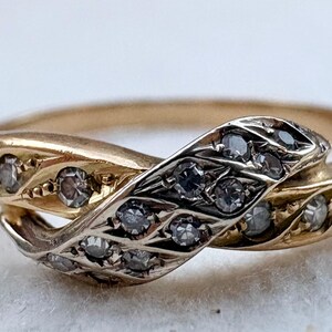 May include: A gold-toned ring in a snake design, with a head and tail that intertwine. The snake's body is adorned with small, round, clear gemstones. The ring's design is detailed and elegant, suitable for jewelry.