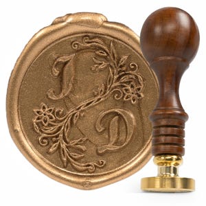 Può includere: Un sigillo di cera dorato con un motivo floreale e le iniziali "J D" impresse su di esso. È incluso un manico in legno con una base in ottone.