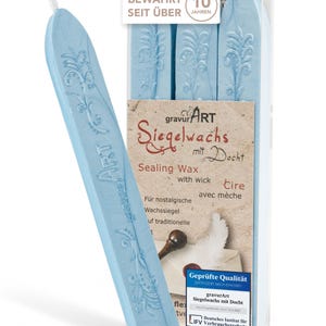 Puede incluir: Barras de cera de sellado azul claro con mecha, empaquetadas en un recipiente de plástico transparente. El embalaje incluye texto en alemán e inglés, con las palabras "gravur ART Siegelwachs mit Docht". Las barras de cera tienen un diseño floral.