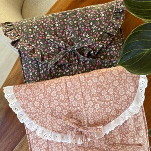 Könnte beinhalten: Zwei gesteppte Stuhlkissen mit Blumenmustern. Das obere Kissen ist grün mit rosa Blumen und einem Rüschenrand. Das untere Kissen ist rosa mit weißen Blumen und einer weißen Spitzenborte.