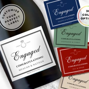 Könnte beinhalten: Eine schwarze Champagnerflasche mit einem individuellen Etikett mit der Aufschrift "Engaged" und "Herzlichen Glückwunsch!" mit den Namen Meagan & Nathan. Zusätzliche Etiketten in verschiedenen Farben werden angezeigt, mit dem Text "30 Farboptionen."