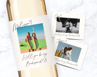 Peut inclure: Une bouteille de vin avec une étiquette affichant une photo de deux femmes avec une planche de surf, le texte "Melissa" et "Will you be my Bridesmaid?" en cursive. Deux photos de style polaroid avec le texte "Sam" et "Jessie" sont également visibles.