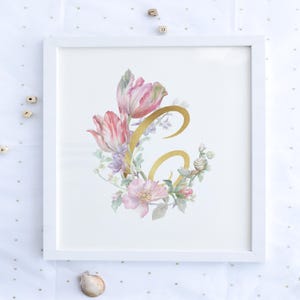 Könnte beinhalten: Ein gerahmter Blumendruck mit einem goldenen Buchstaben "G", umgeben von rosa und lila Blumen und grünen Blättern. Die Blumen umfassen Tulpen und andere Blüten. Der Druck ist in einem weißen Rahmen.