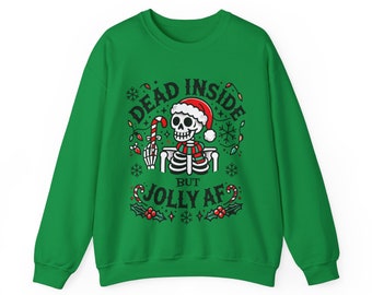 Könnte beinhalten: Ein grünes Sweatshirt mit einem Skelett, das einen Weihnachtsmannhut und einen Schal trägt und eine Zuckerstange hält. Der Text auf dem Sweatshirt lautet "DEAD INSIDE BUT JOLLY AF" in einer festlichen Schriftart mit Stechpalmen- und Schneeflocken-Akzenten.