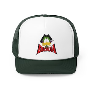 Op de afbeelding: Een witte truckercap met een groene eend die een cape draagt en een rood "Count Duckula" logo op de voorkant. De pet heeft een donkergroen mesh achterkant.