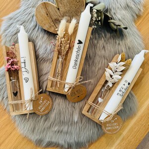 Può includere: Tre portacandele in legno con candele bianche, ognuno con un piccolo flacone di vetro contenente fiori secchi. I portacandele hanno le parole "Danke schön", "Danke" e "Vielen Dank" scritte su di essi. Ogni portacandele ha un piccolo cartellino con le parole "Ein herzliches Dankeschön" scritte su di esso.