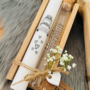 K&ouml;nnte beinhalten: Eine wei&szlig;e Kerze mit einer Autoillustration und Herzen, ein Glasfl&auml;schchen mit Korken und ein kleiner Strau&szlig; wei&szlig;er Blumen werden in einer Holzkiste pr&auml;sentiert. Der Text "von HERZEN" befindet sich auf einem braunen Etikett.