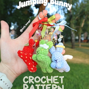 May include: Three crochet bunny keychains featuring red, green, and blue yarn textures with decorative ribbons, beads, and charms. The text Jumping Bunny CROCHET PATTERN Three Designs is visible. Each bunny has distinct details like a strawberry pattern.