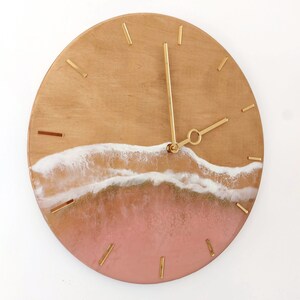 May include: A round wooden clock with gold hands and a pink and white resin wave design.