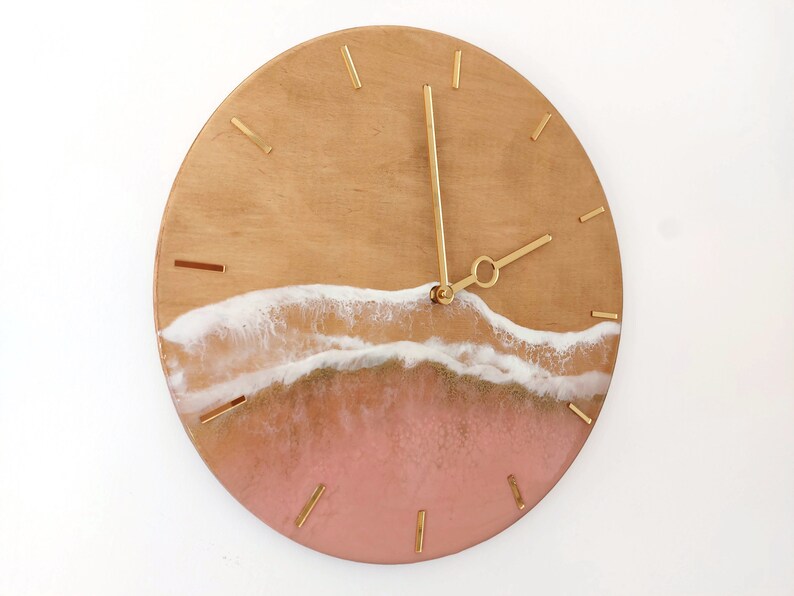 May include: A round wooden clock with gold hands and a pink and white resin wave design.