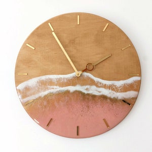 May include: A round wooden clock with gold hands and a pink and white resin wave design.