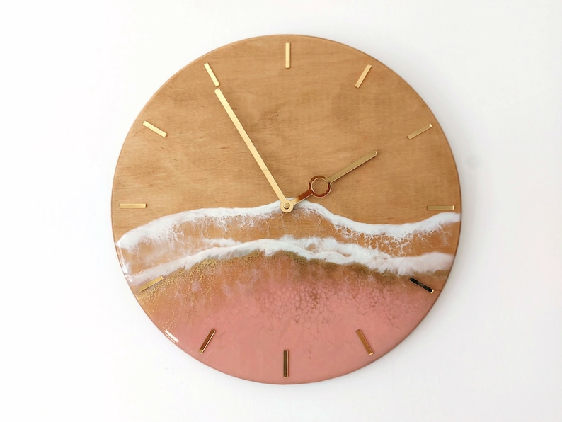 May include: A round wooden clock with gold hands and a pink and white resin wave design.