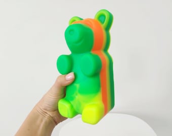 May include: A green, yellow and orange gummy bear shaped like a teddy bear. The bear is standing upright and has a friendly expression.