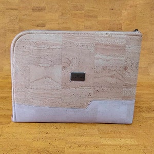 May include: A light pink and purple cork laptop sleeve with a zipper closure. The sleeve has a small silver logo that says "Cork & Tree".