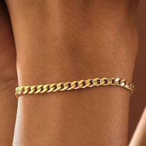 May include: A gold-colored curb chain bracelet. The bracelet is made of small, interlocking links. The bracelet is worn on a wrist.