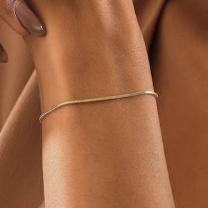 Könnte beinhalten: Ein goldenes Kettenarmband am Handgelenk einer Person. Das Armband ist dünn und zart, mit einem schlichten Design.