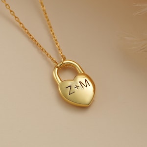 May include: A gold necklace with a heart-shaped padlock pendant. The padlock has the initials "Z+M" engraved on it.
