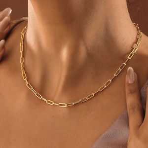 May include: A gold chain necklace with a simple, linked design. The necklace is worn by a person with a light complexion.