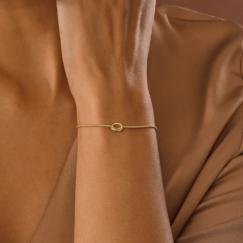 Peut inclure: Un bracelet en or avec un petit charme rond nou&eacute;. Le bracelet est fin et d&eacute;licat, et le charme est simple et &eacute;l&eacute;gant.