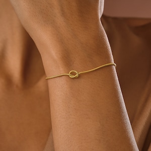 Peut inclure: Un bracelet en cha&icirc;ne dor&eacute;e avec un motif de n&oelig;ud. Le bracelet est port&eacute; au poignet.